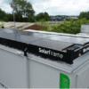 Black SolarFrame mounting rail labeled SolarFrame on top of a gray industrial container in an outdoor lot.