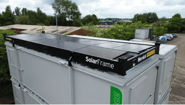 Black SolarFrame mounting rail labeled SolarFrame on top of a gray industrial container in an outdoor lot.