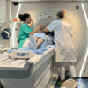 Patient on an examination table is assisted by two clinicians beside an MRI machine in a hospital room, preparing for scanning ground truth image context.
