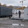Un groupe électrogène et une batterie mobile sur un chantier, avec une responsable préparant leur utilisation — illustration